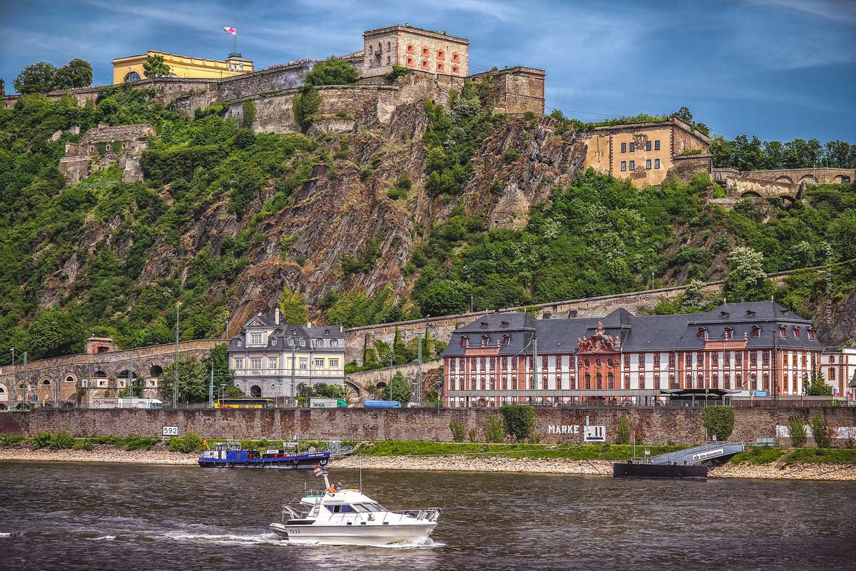 Blick auf den Rhein mit den vielen charmanten Häusern des Rheinlandes am Ufer, einer Burg oben auf dem Berg und kleinen Booten auf dem Wasser