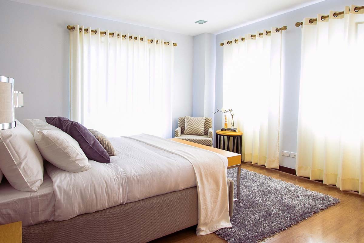 Modernes Schlafzimmer mit Doppelbett und großen Fenstern, durch die helles Licht kommt