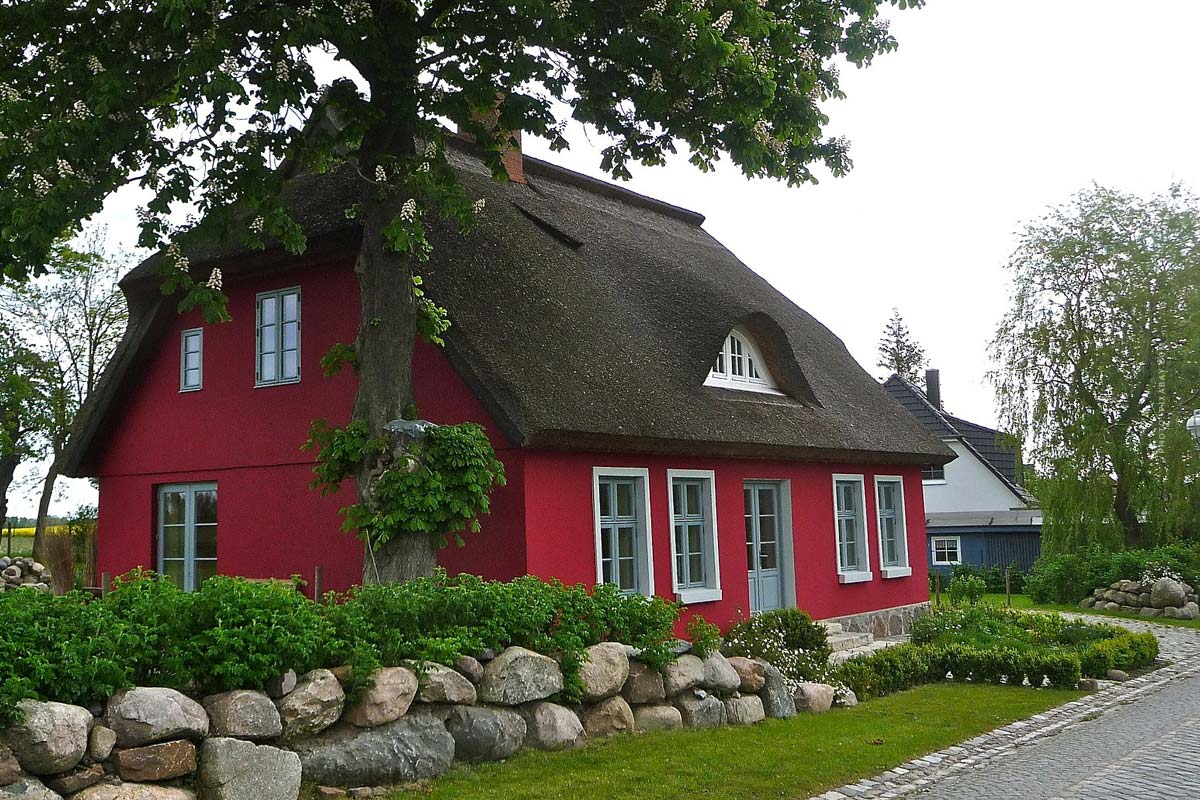 Traditionelles Einfamilienhaus mit Garten und Terrasse und roter Fassade in idyllischer Landschaft 