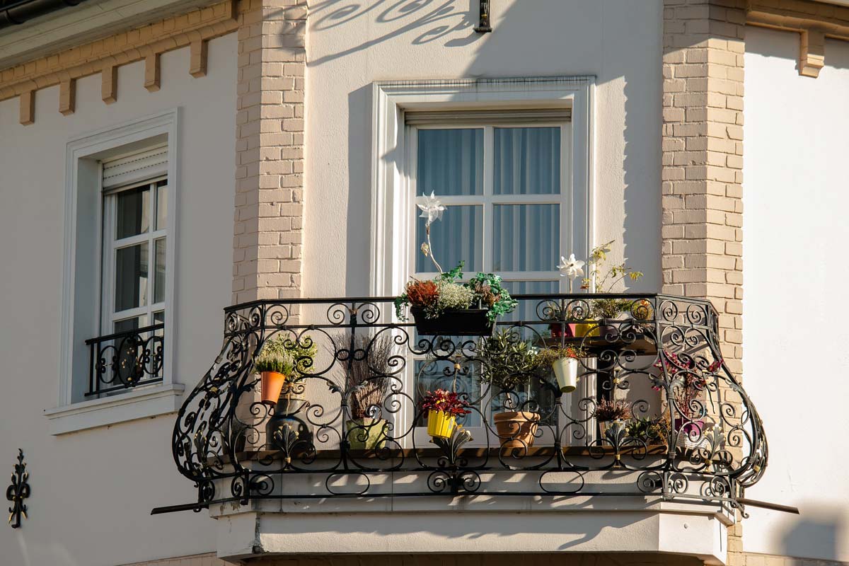 Balkon eines Mehrfamilienhauses vor großem, weißen Fenster mit Pflanzen