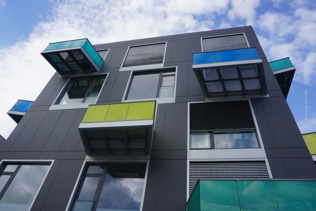 Modernes Mehrfamilienhaus mit großen Fenstern und bunten Balkonen vor strahlend blauem Himmel